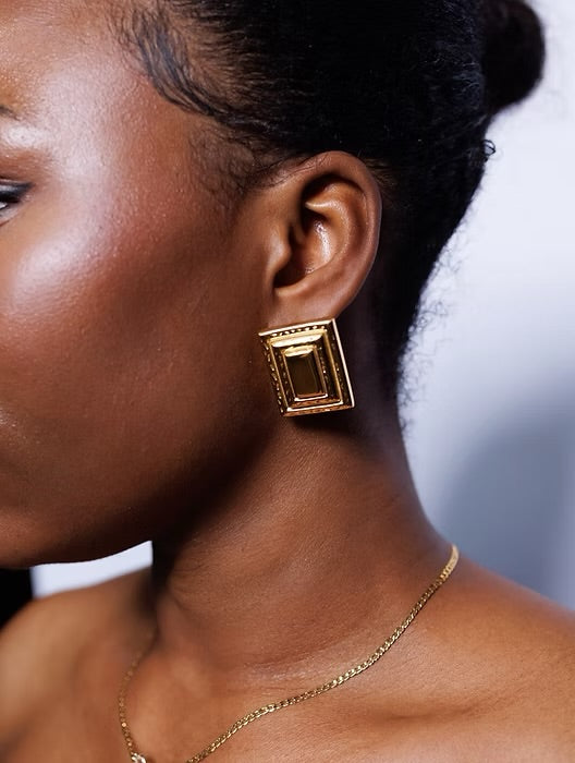 Close-up of a person wearing gold earrings and a necklace against a blurred background