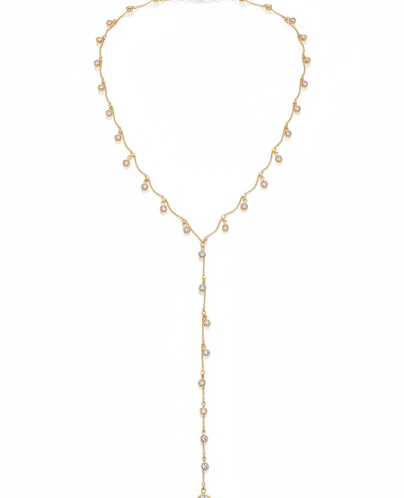 A close-up lifestyle shot of a model wearing a deep plum halter top with a plunging V-neckline, styled with a delicate gold Y-necklace featuring small clear crystal charms.