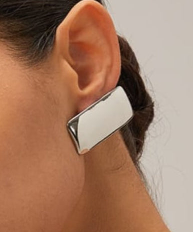 Close-up of a person wearing a silver earring on a plain background