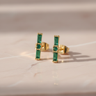 Gold earrings with green gemstones on a beige surface