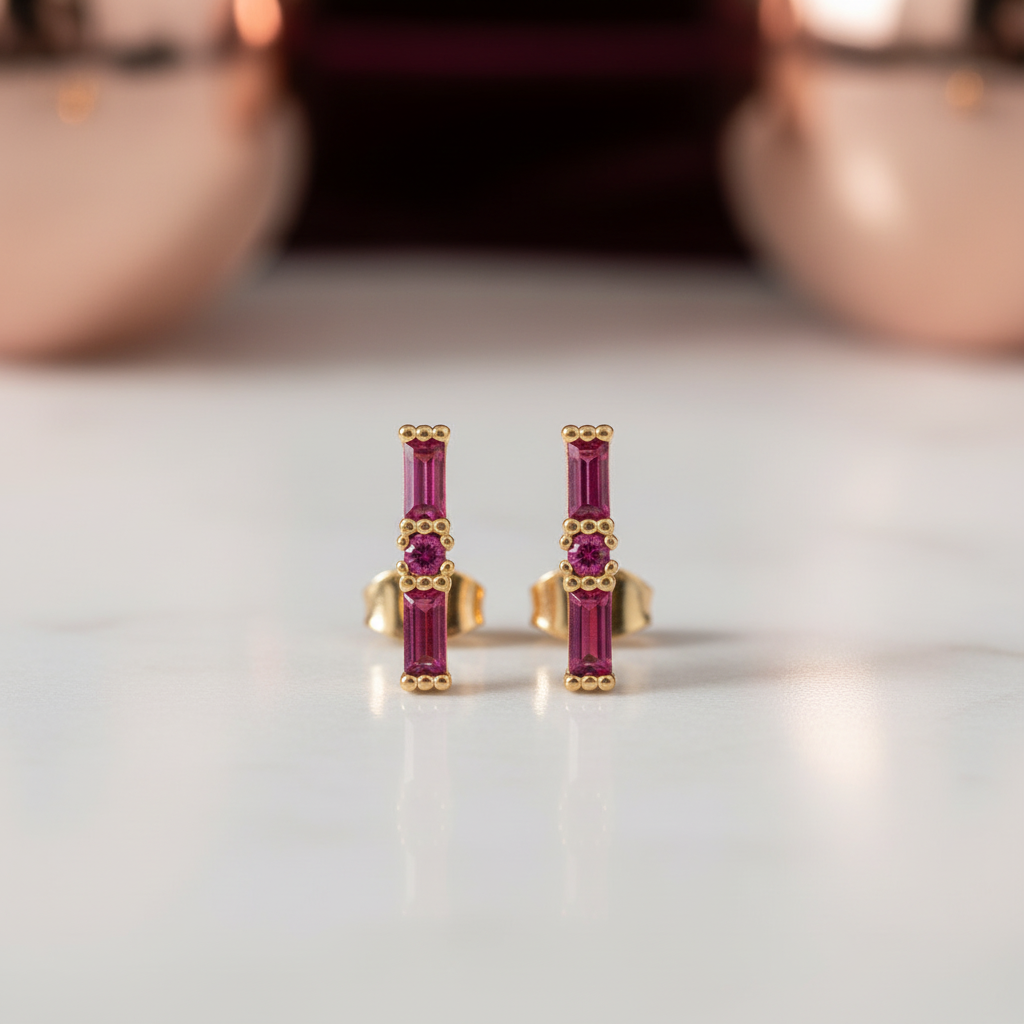 Gold earrings with red gemstones on a reflective surface