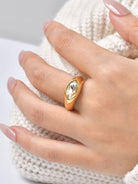 A gold signet-style ring with a clear oval gemstone worn on a person's hand, resting against a cream-colored knit sweater.