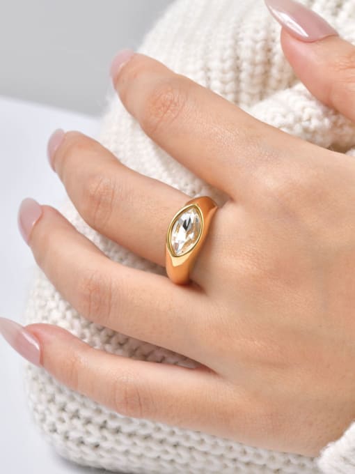 A gold signet-style ring with a clear oval gemstone worn on a person's hand, resting against a cream-colored knit sweater.