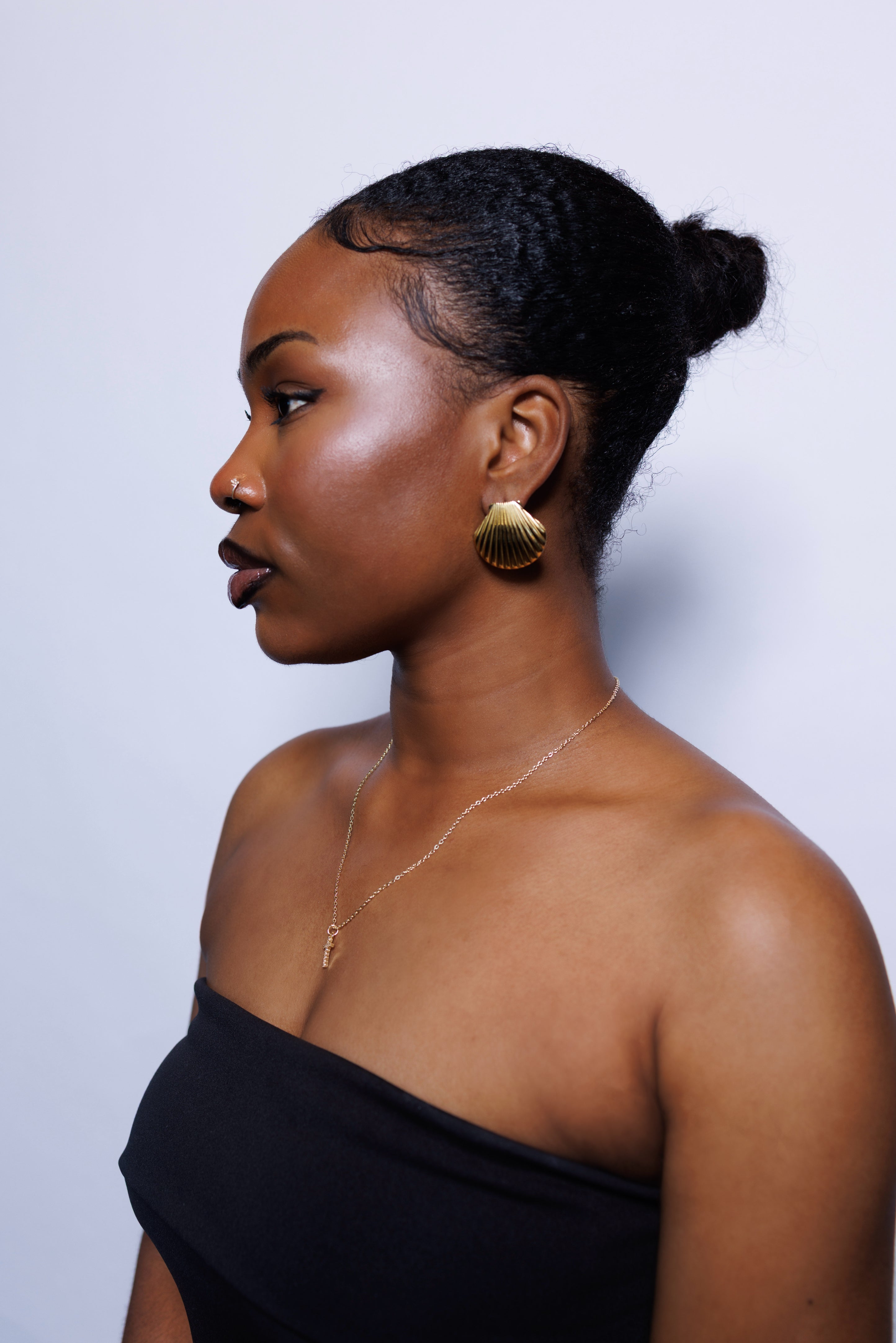 Woman wearing gold earrings and a black top against a light background