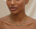Woman wearing a gold and green necklace against a neutral background