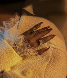 Hand with red nail polish wearing multiple rings on a textured surface