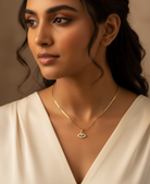 Woman wearing a gold necklace with an eye pendant against a neutral background