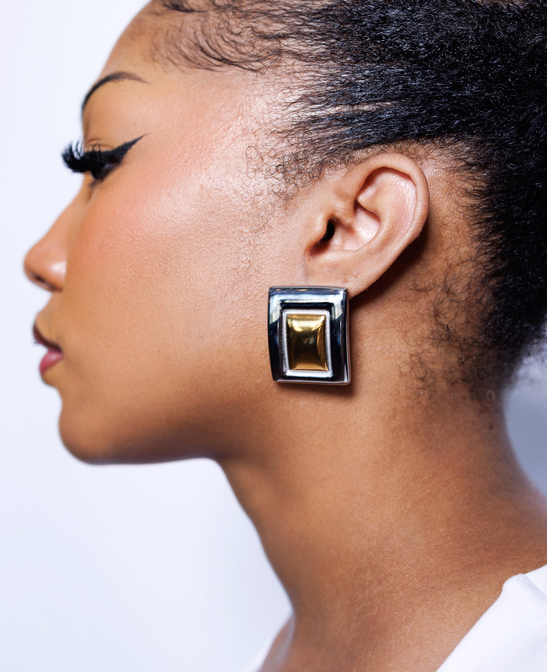 Close-up of a woman wearing a gold and silver earring against a neutral background