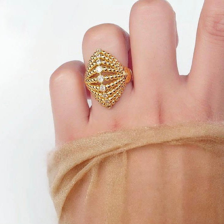 Gold ring with a textured design worn on a finger against a white background