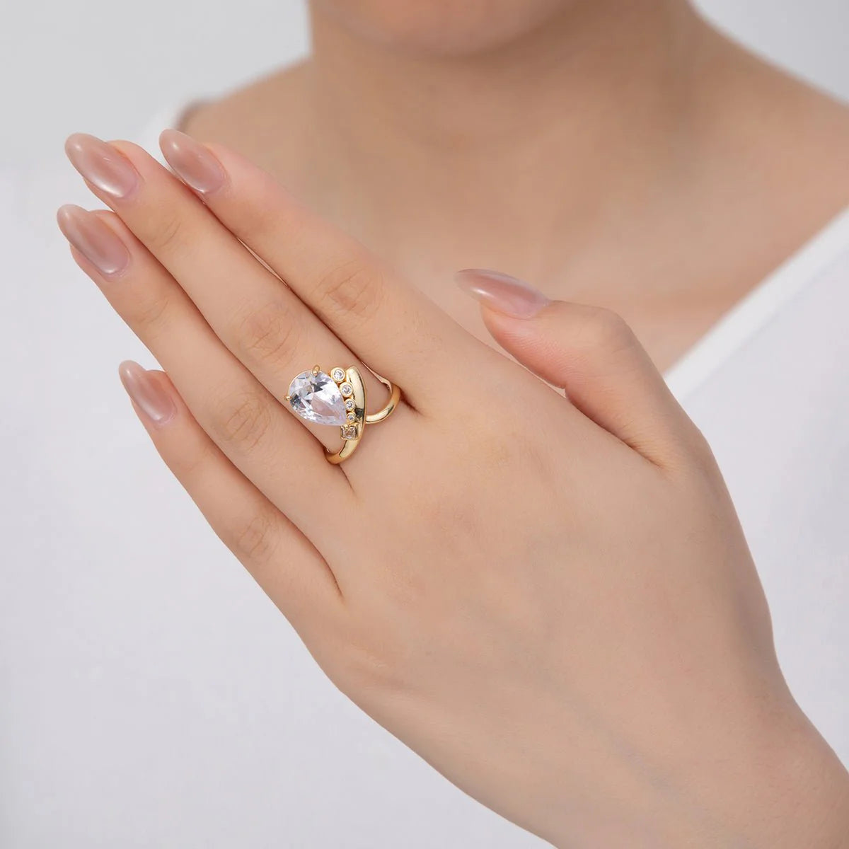 Hand wearing a gold ring with a heart-shaped gemstone on a plain background