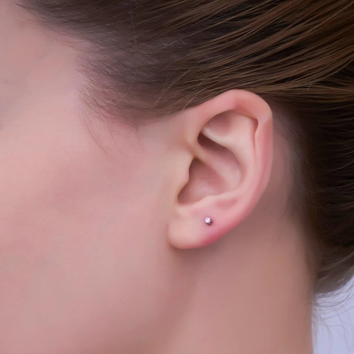 Close-up of an ear with a small earring on a neutral background