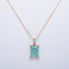 Gold pendant with a rectangular turquoise stone on a light gray background
