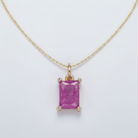 Gold pendant with a pink gemstone on a light gray background