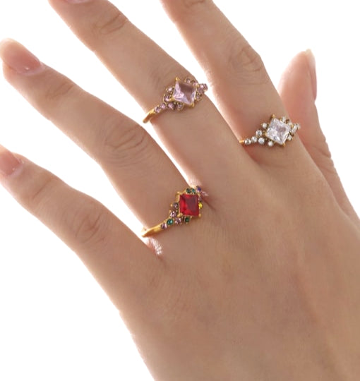 Hand wearing three decorative rings with gemstones on a white background
