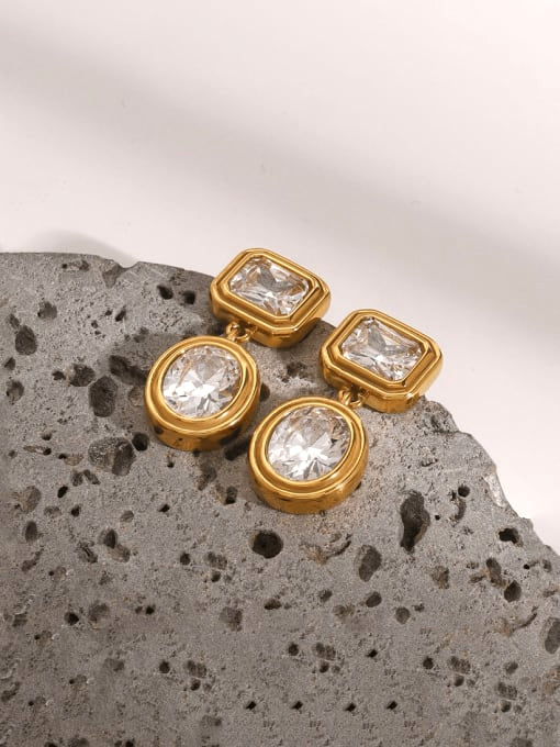 Gold earrings with clear gemstones on a textured stone surface