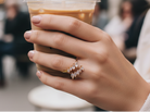 Hand holding a cup of coffee wearing a clear gemstone ring with a blurred city street background