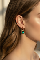 Close-up of a woman wearing emerald green earrings with a neutral background