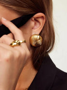 Close-up of a person wearing gold earrings and a ring, with a blurred background.
