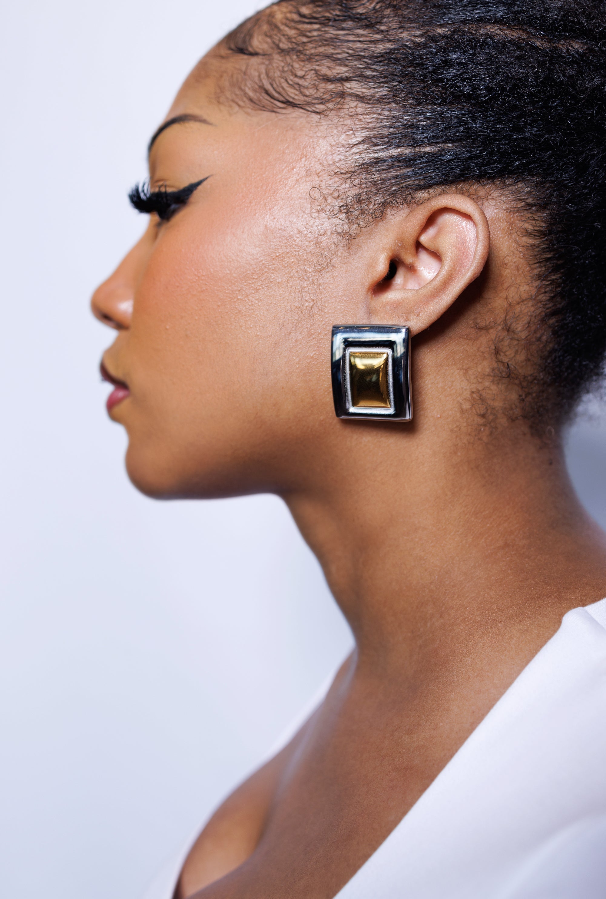 Close-up of a woman wearing a gold earring against a light background