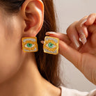 Gold earrings with eye design worn by a person