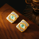 Gold and green eye-shaped earrings on a brown surface