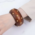 Wooden bracelet with gold star and circle studs on a wrist against a light background