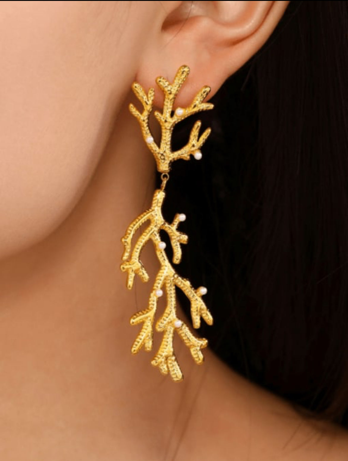 Gold leaf-shaped earrings worn by a person with a dark background