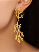 Gold leaf-shaped earrings worn by a person with a dark background