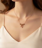 Gold necklace with a bow-shaped pendant worn by a model in a white top.