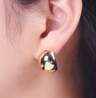 Gold and black earring worn on an ear with a blurred background