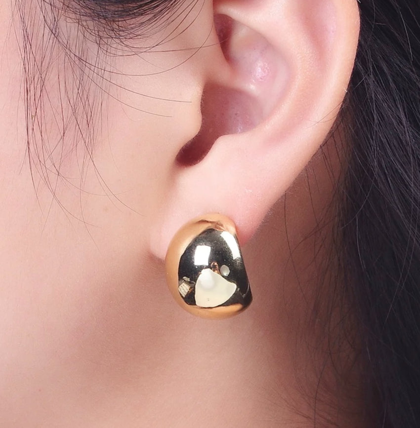 Gold and black earring worn on an ear with a blurred background