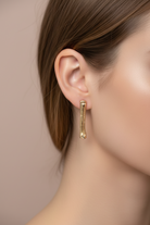 A close-up side profile of a woman wearing a slim, textured gold drop earring.