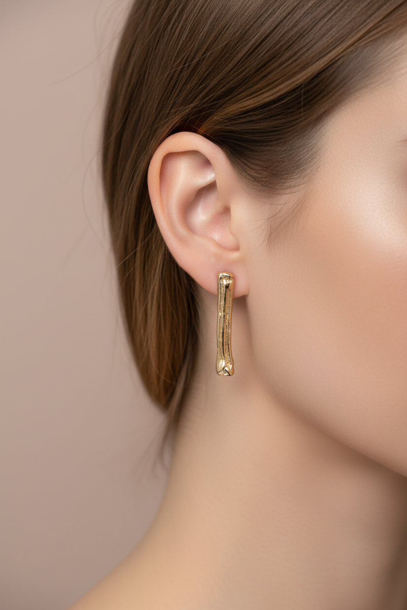 A close-up side profile of a woman wearing a slim, textured gold drop earring.