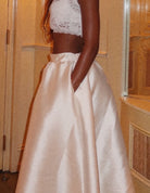 Person wearing a white lace top and beige skirt in a bathroom setting