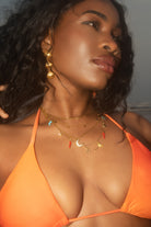Woman wearing an orange bikini with gold jewelry against a neutral background