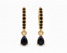 A pair of gold huggie hoop earrings with small black stones along the front and a teardrop-shaped black gemstone dangling from the center, shown on a plain white background.