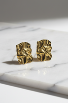 Gold leaf-shaped earrings on a marble surface
