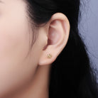 Close-up of an ear wearing a gold stud earring with a dark background