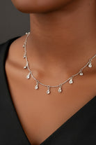 Silver necklace with small pendants on a person wearing a black shirt.