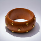 Brown wooden bangle with gold studs on a white background