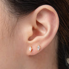 Close-up of an ear wearing gold earrings with clear gemstones.