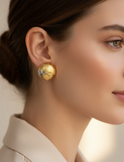 Close-up of a person wearing gold earrings with a neutral background