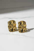 Gold leaf-shaped earrings on a marble surface