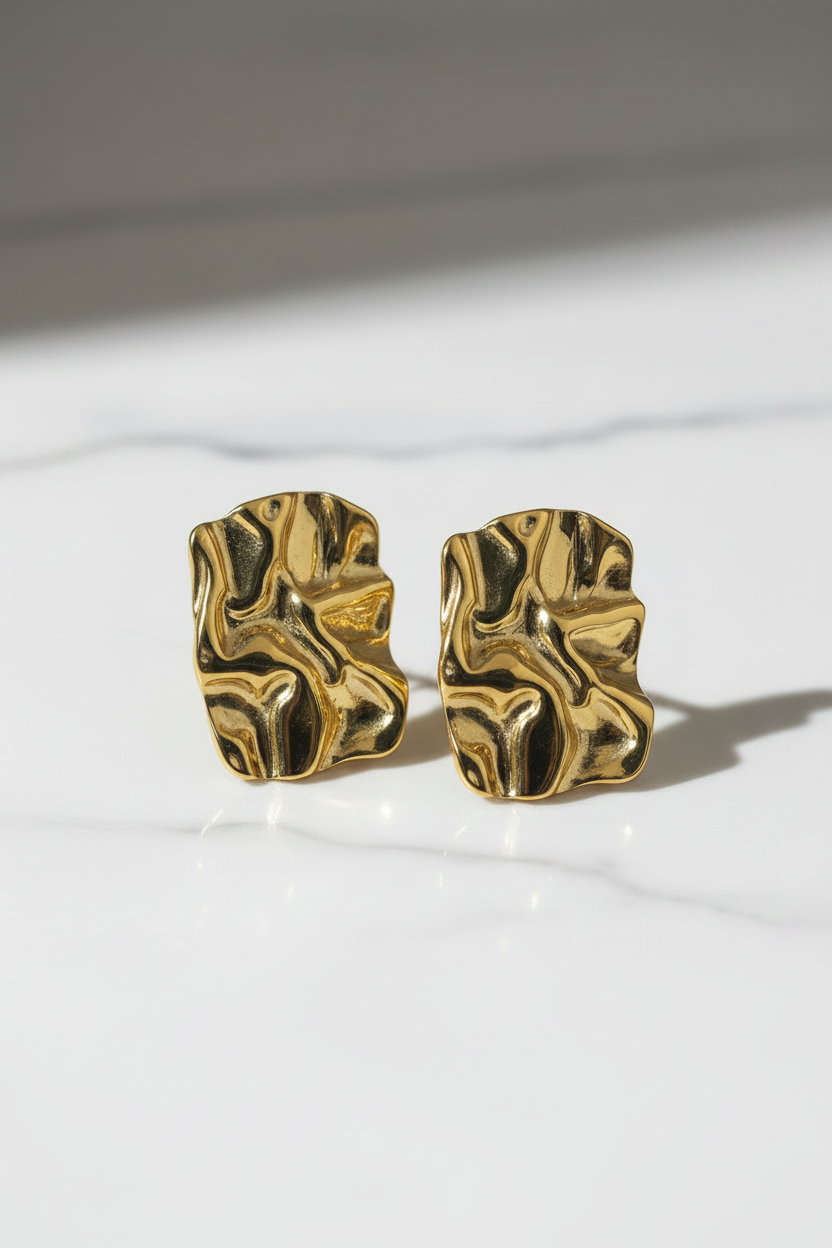 Gold leaf-shaped earrings on a marble surface