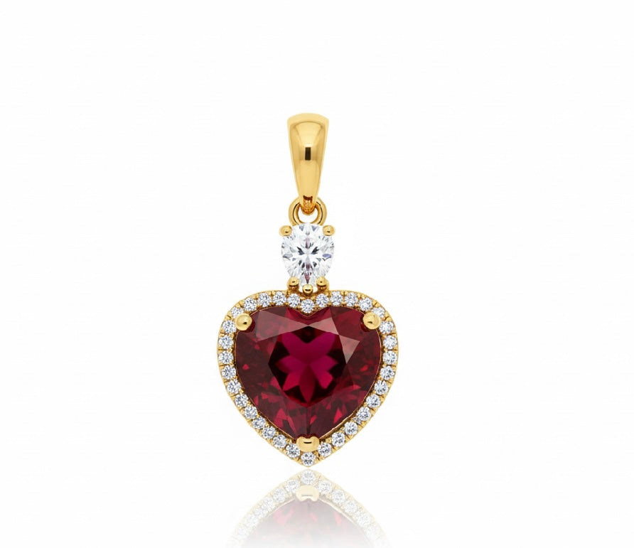 Gold pendant with a heart-shaped red gemstone and clear stones on a white background