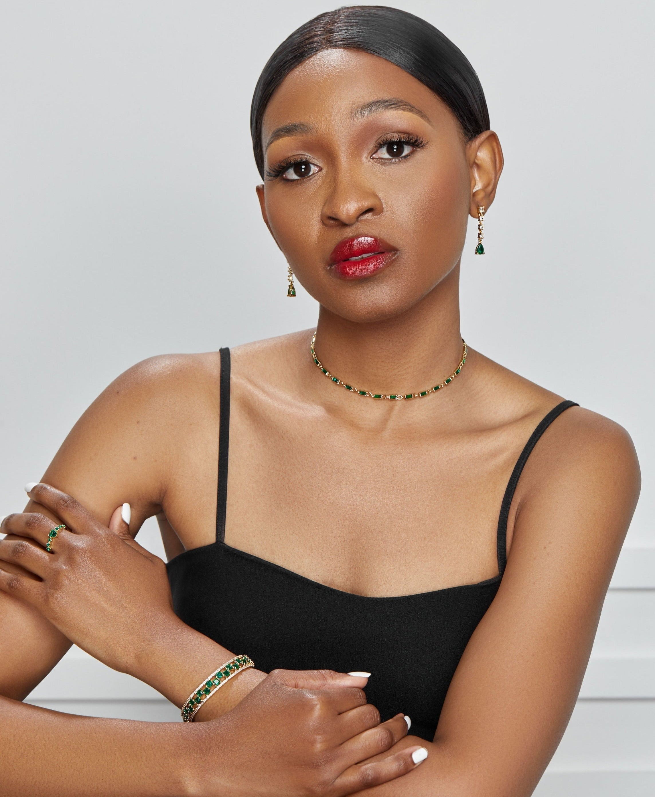 Woman wearing a black dress with green jewelry against a white background