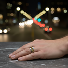 Hand wearing a gold ring with blurred city lights in the background