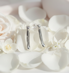 A pair of polished silver drop earrings with a textured vertical bar design, resting on white rose petals.