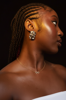 Woman with braided hair wearing earrings and a necklace against a dark background