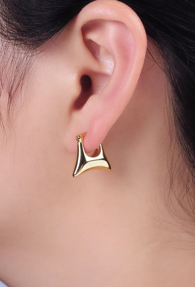 Gold earring worn on a person's ear with a blurred background